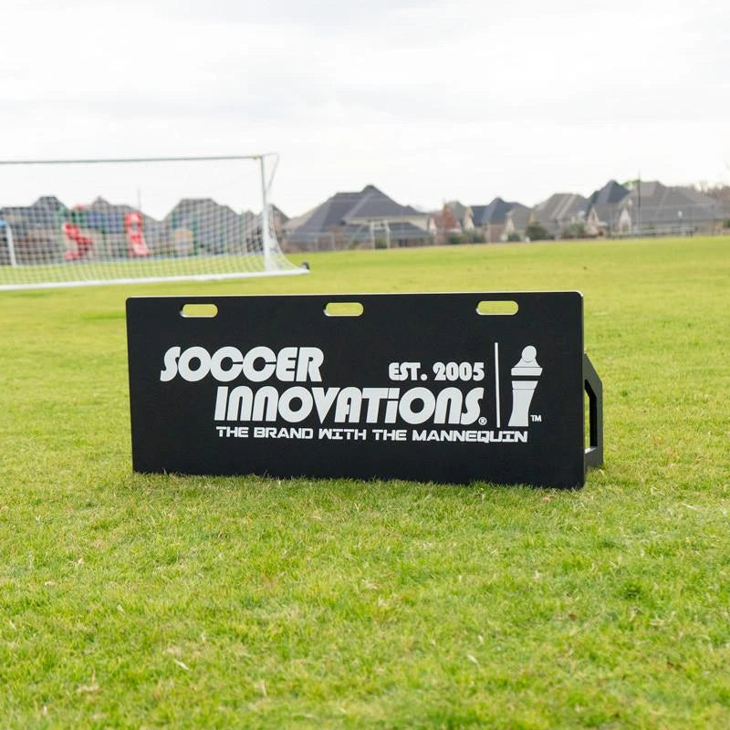 Soccer rebounder board at angle on grass showing adjustable tilting feature for training passes